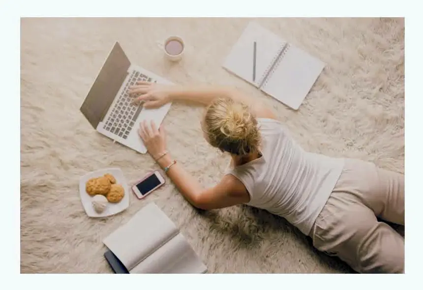 Young blogger working on the floor surrounded by their laptop, phone, coffee, books, etc